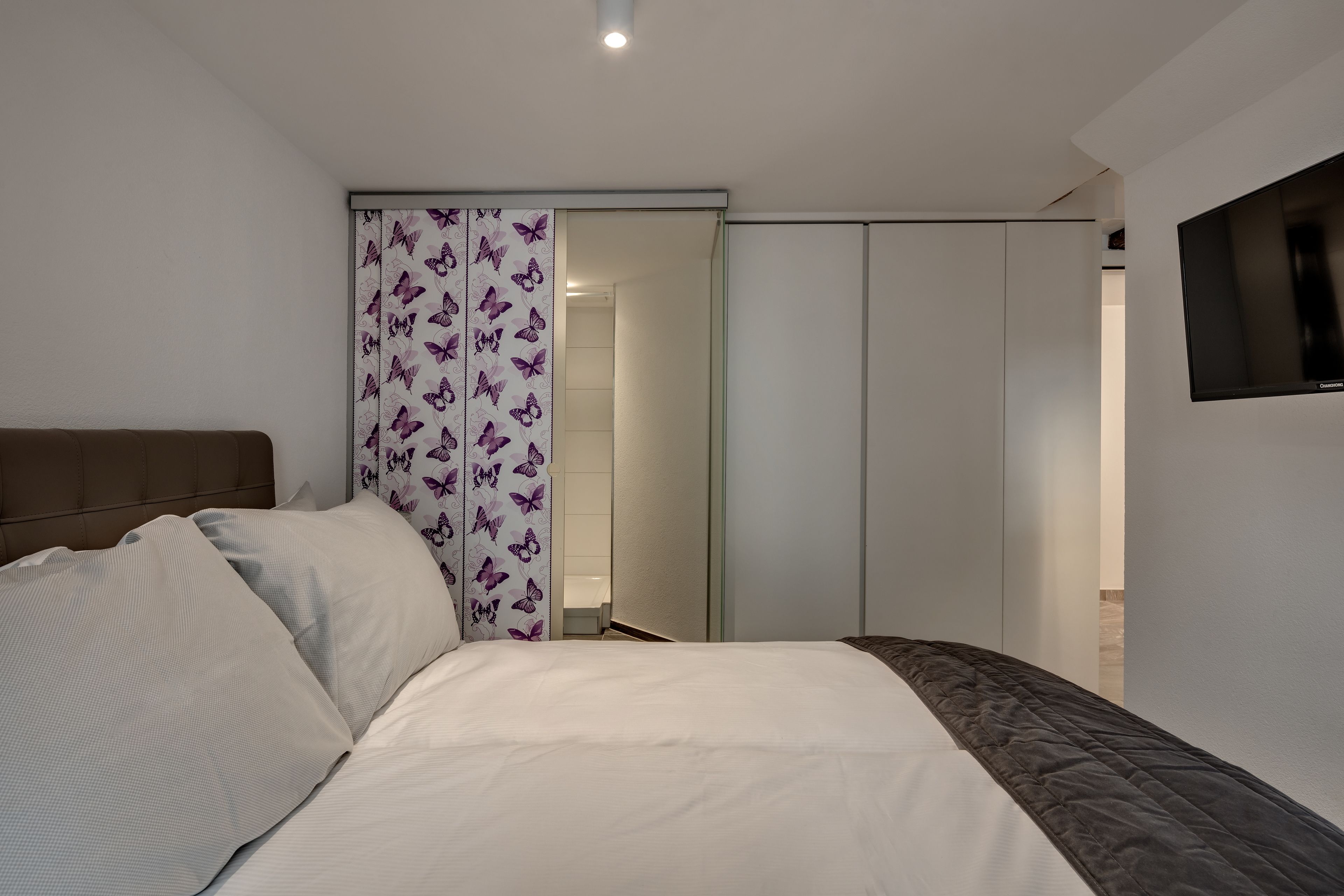 A bedroom with a bed, a wardrobe, and a television on the wall.