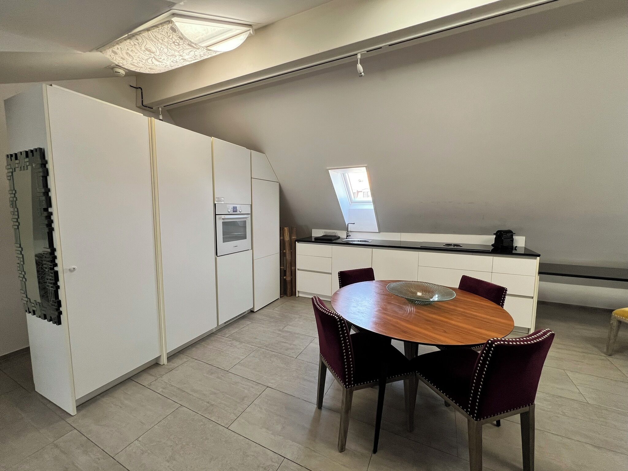 A modern kitchen with a built-in oven, a dining table with chairs, and a large window providing natural light.
