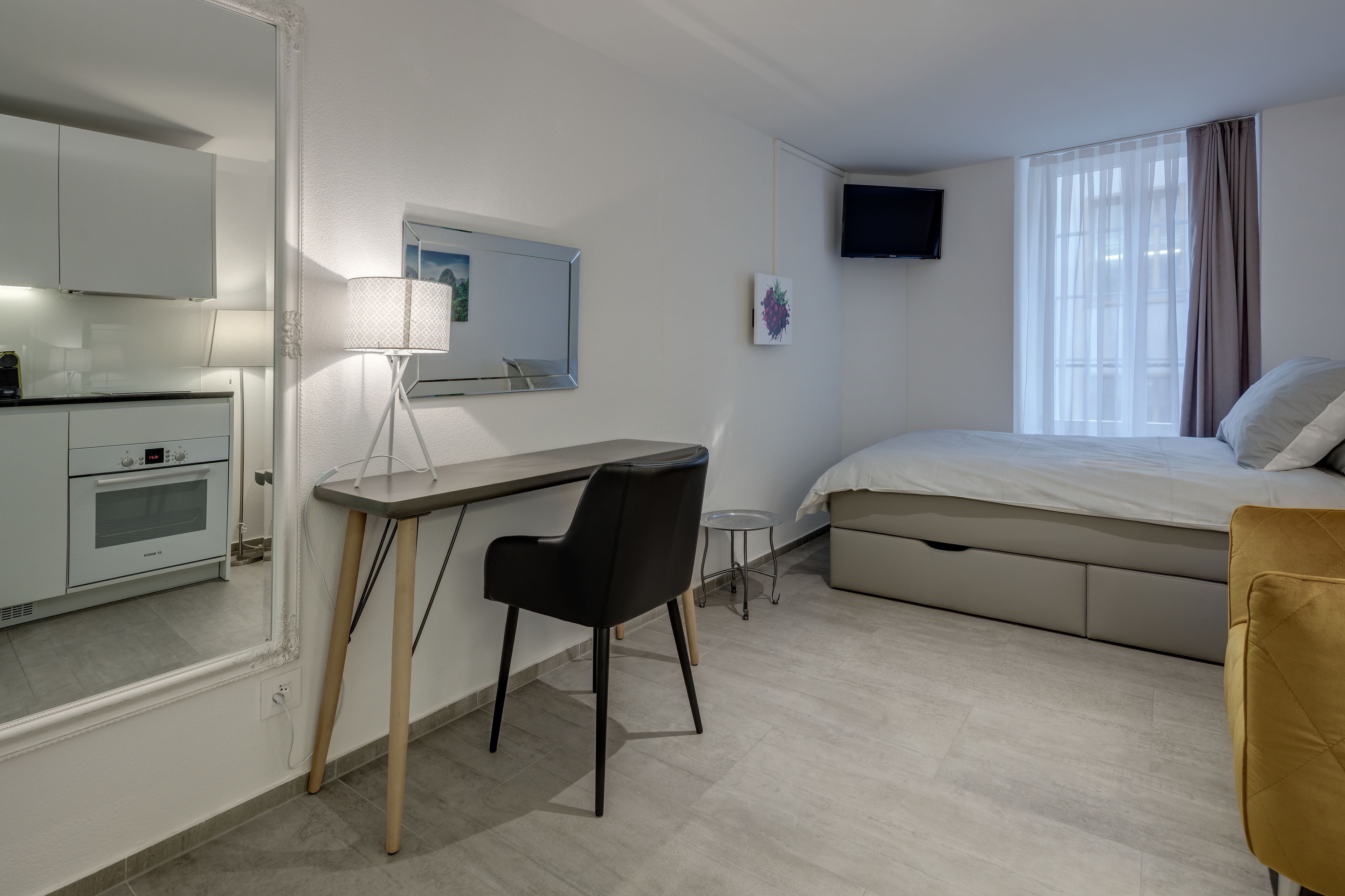 Ett modernt hotellrum med en säng, ett skrivbord, en stol, ett litet bord, en tv och ett fönster med gardiner.