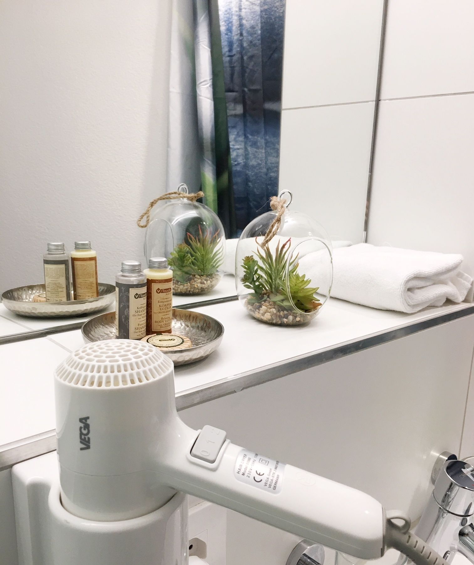 A bathroom with a white countertop, a hairdryer, and decorative glass terrariums with plants.