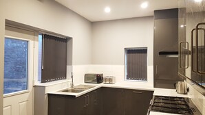 A compact kitchen with dark cabinets, a stainless steel sink, a toaster, and a stove. - Central City House (Liverpool)