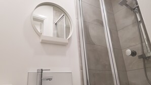 A modern bathroom with a round mirror, a glass-enclosed sink, and a walk-in shower with a glass door. - Central City House (Liverpool)