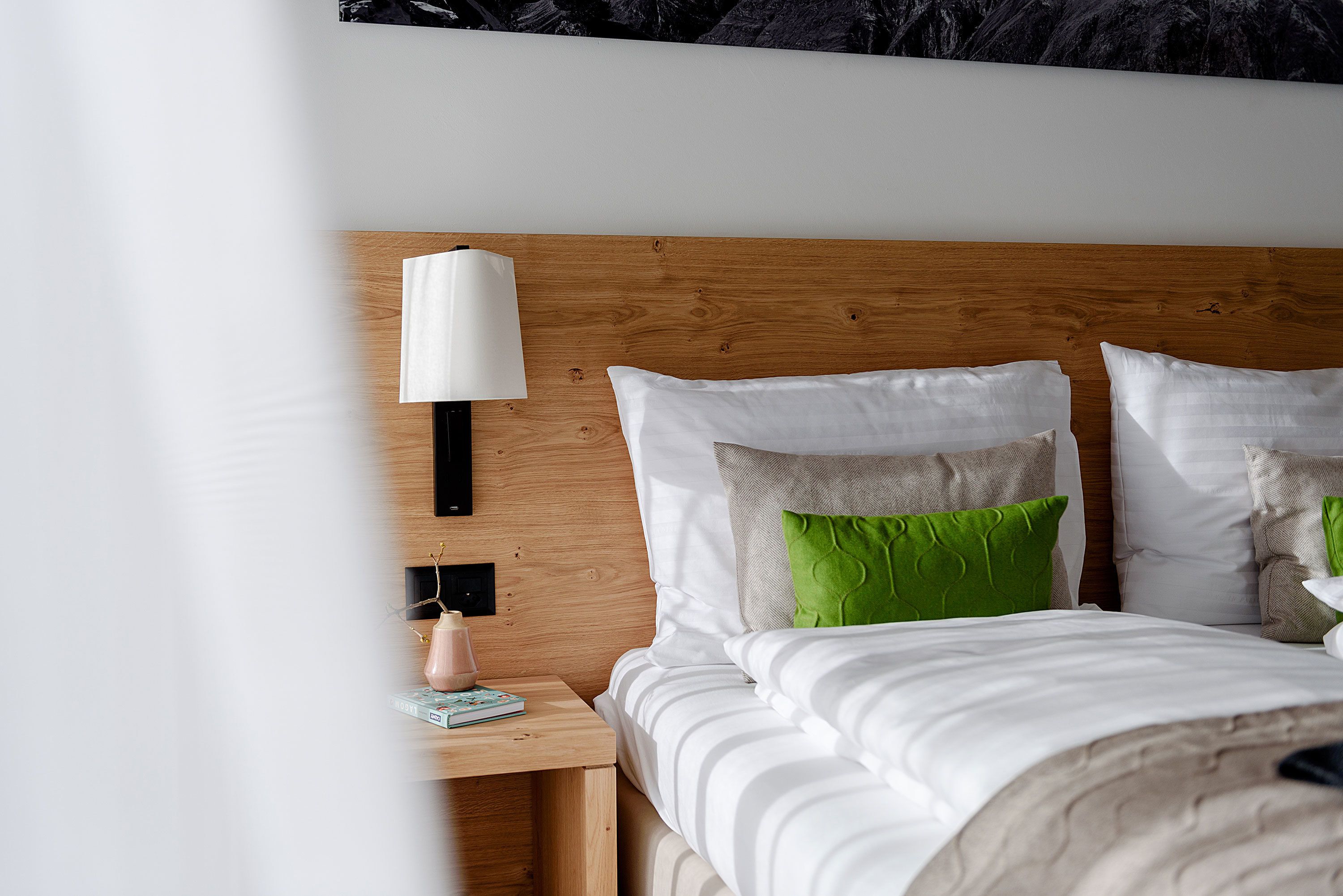 Una cama bien hecha con almohadas blancas y verdes, un cabecero de madera y una lámpara de noche.