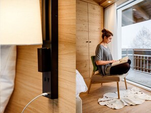 A modern room with a wooden floor, a green chair, a white blanket, and a window with a view of a snowy landscape.