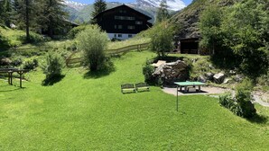A mountain lodge with a view of a snow-capped peak, surrounded by lush greenery and a wooden fence. - EVA Apartments (Zermatt)