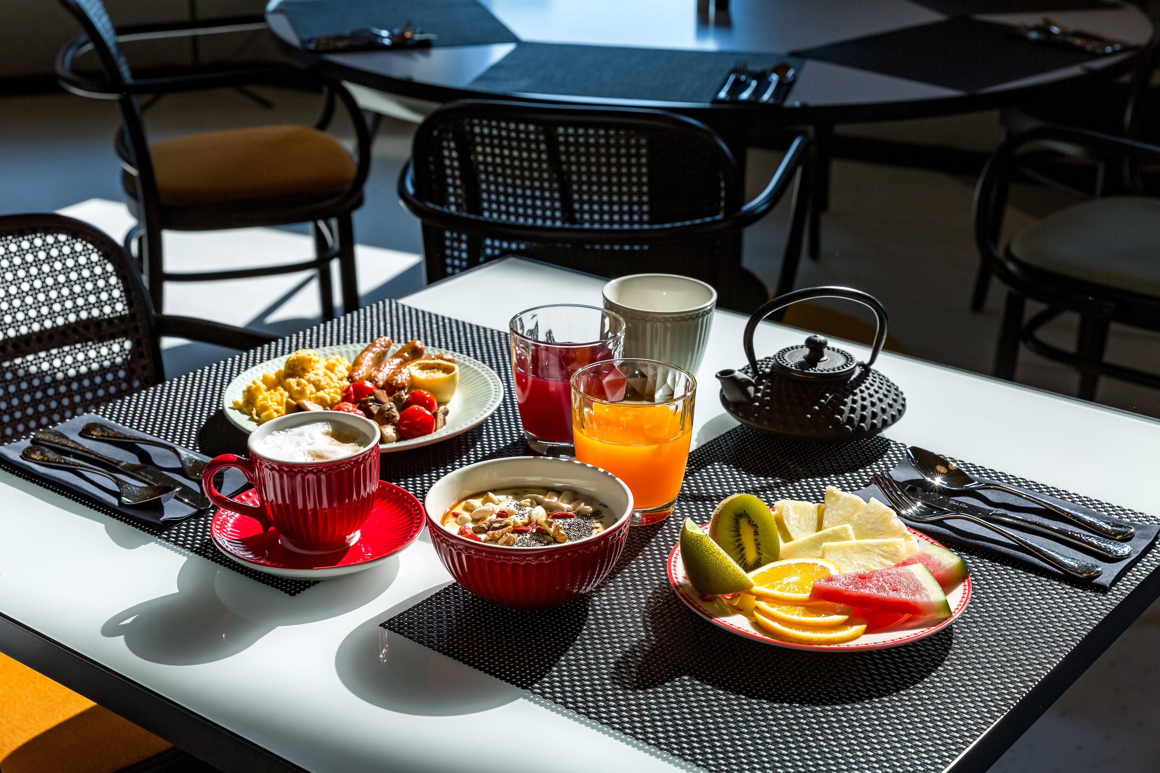Een ontbijttafel met een kom ontbijtgranen, een kop koffie, een glas sinaasappelsap en een schaal fruit.