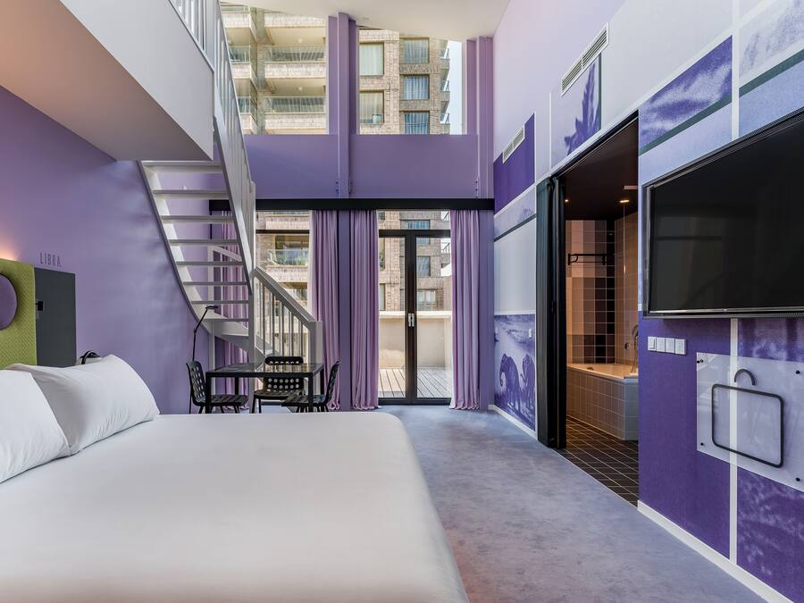A modern hotel room with a bed, a desk, and a staircase leading to an upper level.