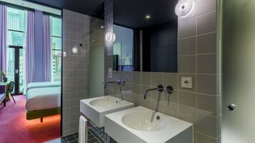 Une salle de bain moderne avec deux lavabos, un grand miroir et une vue sur le paysage urbain, visible à travers une porte en verre.