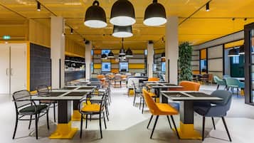 A modern dining area with tables and chairs, a yellow ceiling, and a large plant.