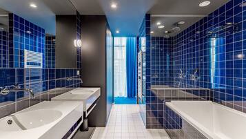 Un bagno moderno con due ampi lavabi bianchi, una vasca e pareti rivestite di piastrelle azzurre.