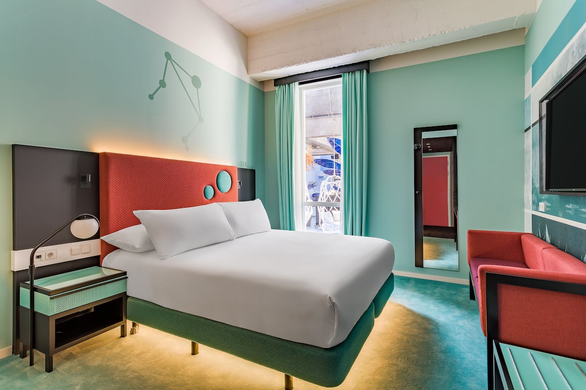 Une chambre d’hôtel équipée d’un lit, d’un bureau, d’une chaise, d’une télévision et d’une fenêtre avec des rideaux.