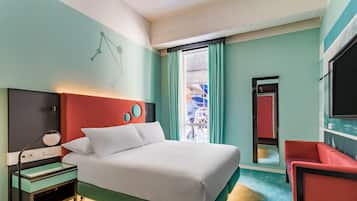 Habitación de hotel con cama, escritorio, silla, televisor y ventana con cortinas.