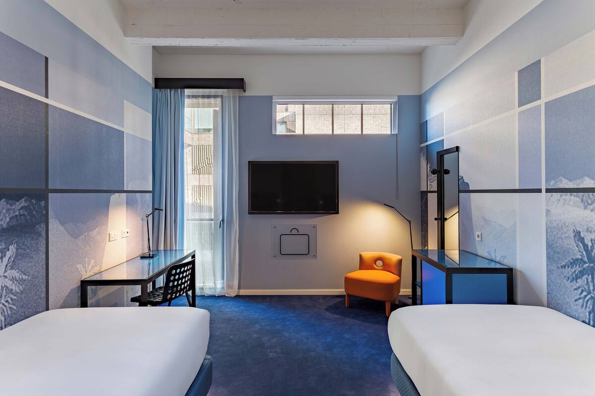 Une chambre d’hôtel avec deux lits, un bureau, une chaise, une télévision et une fenêtre.