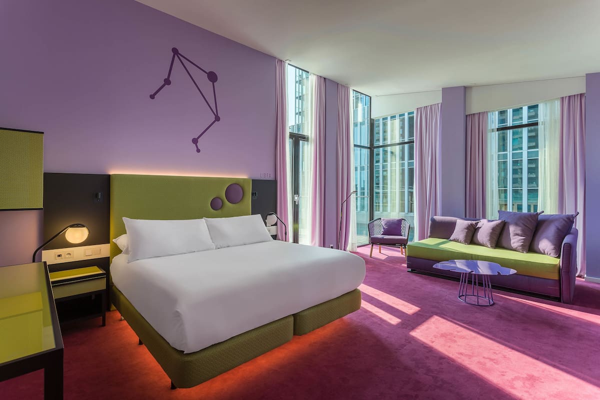 Une chambre d’hôtel moderne avec un grand lit, un canapé vert et une petite table.