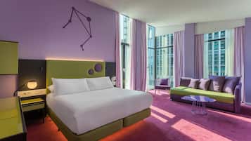 Una habitación de hotel moderna con una cama grande, un sofá verde, una mesita pequeña y una obra de arte colgada en la pared.