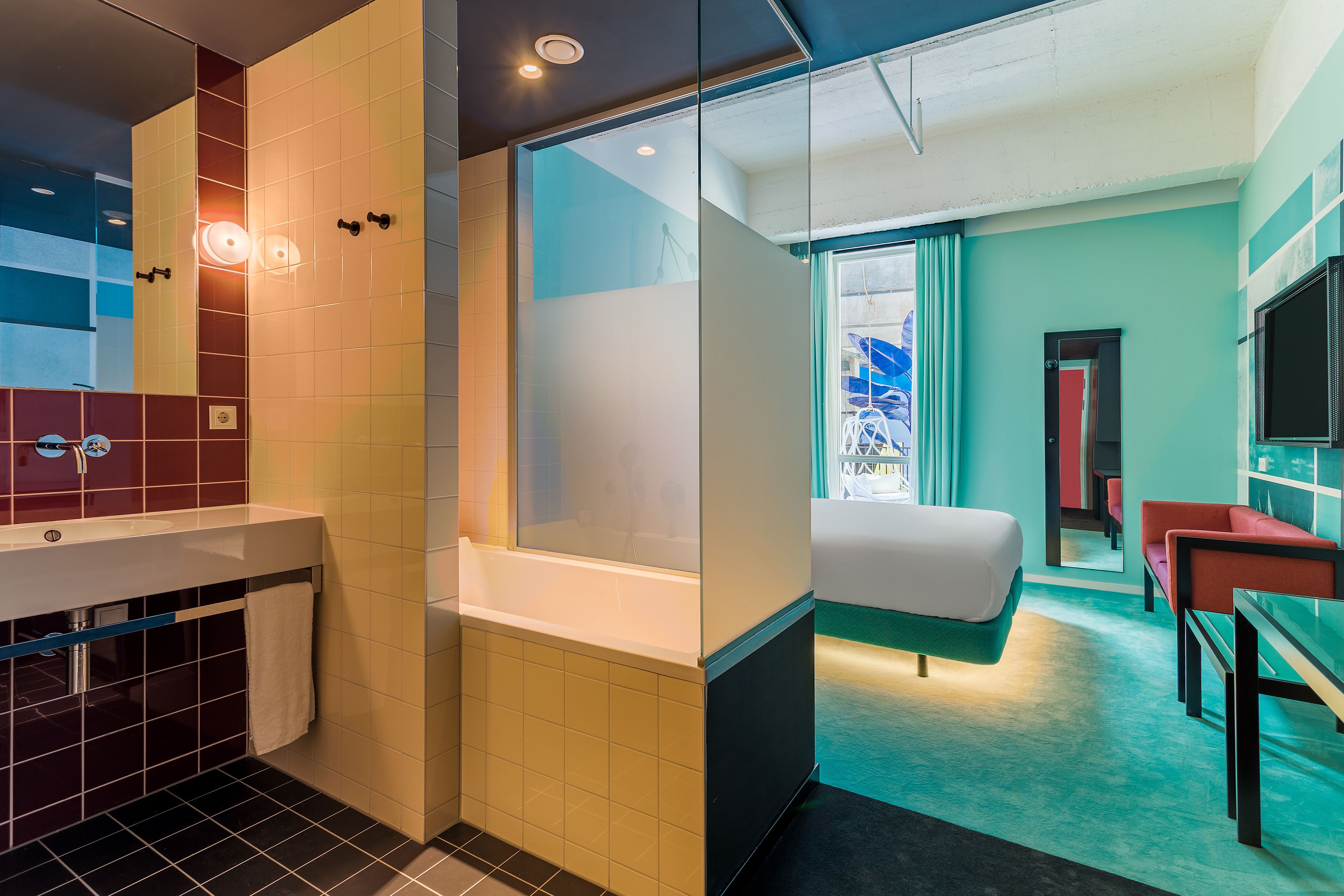 A modern hotel room with a large window, a separate bathroom, a bed, a desk, and a TV.