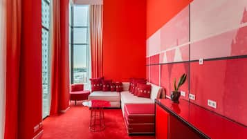 A modern room with a red carpet, a sofa with matching cushions, a small table, and a potted plant.