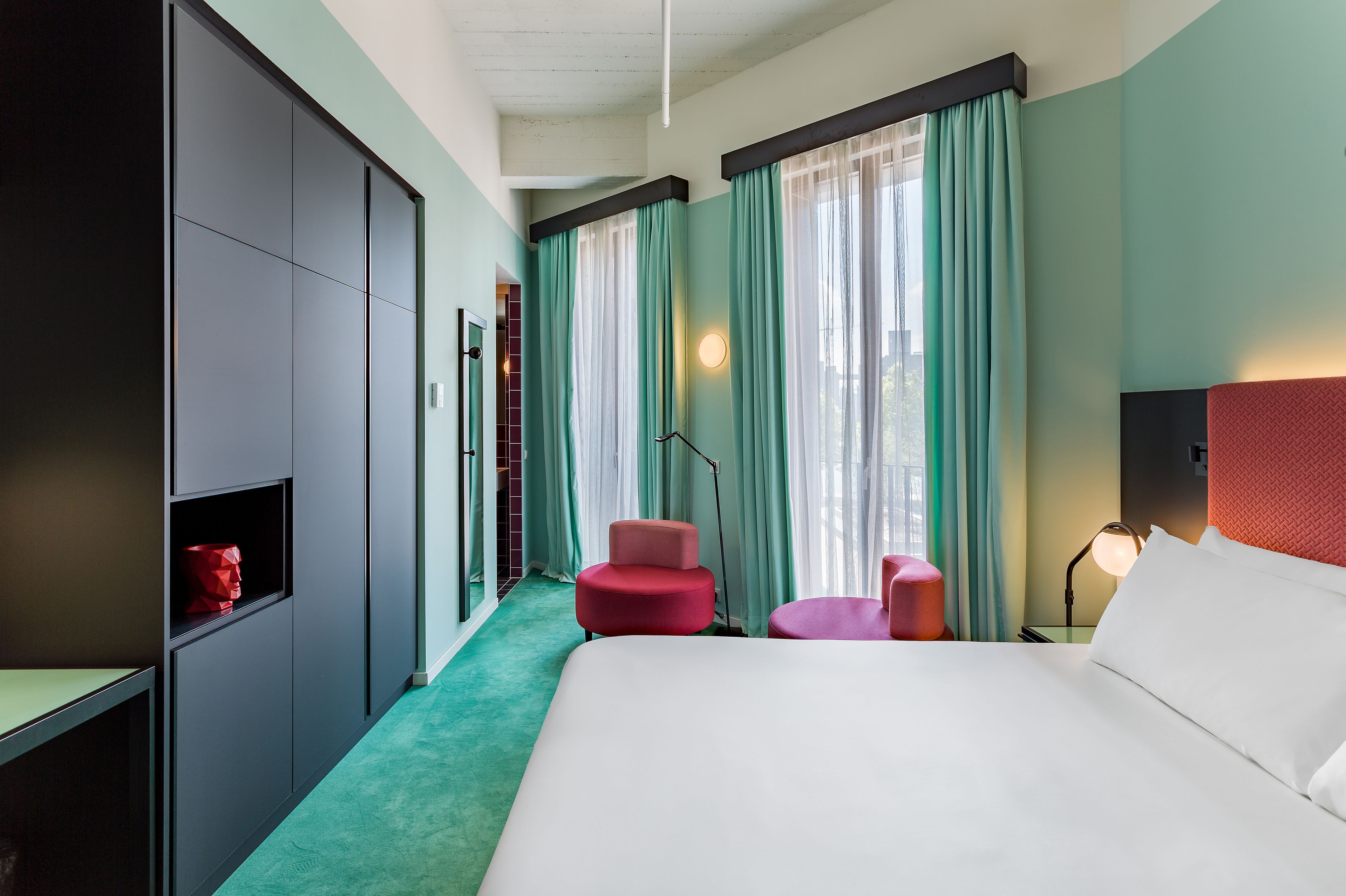 Una habitación de hotel con una cama grande, dos sillas rojas, un escritorio y un armario.