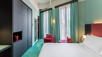 Una habitación de hotel con una cama grande, dos sillas rojas, un escritorio y un armario.