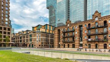 Een modern stedelijk gebied met een combinatie van hoge en lage gebouwen, waaronder een opvallend gebouw van baksteen met balkons en een groot glazen gebouw op de achtergrond.