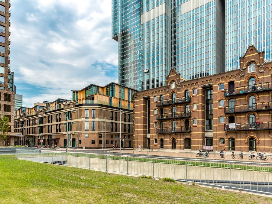 Un área urbana moderna con una combinación de edificios altos y bajos, incluyendo un destacado edificio de ladrillo con balcones y un gran edificio de vidrio al fondo.