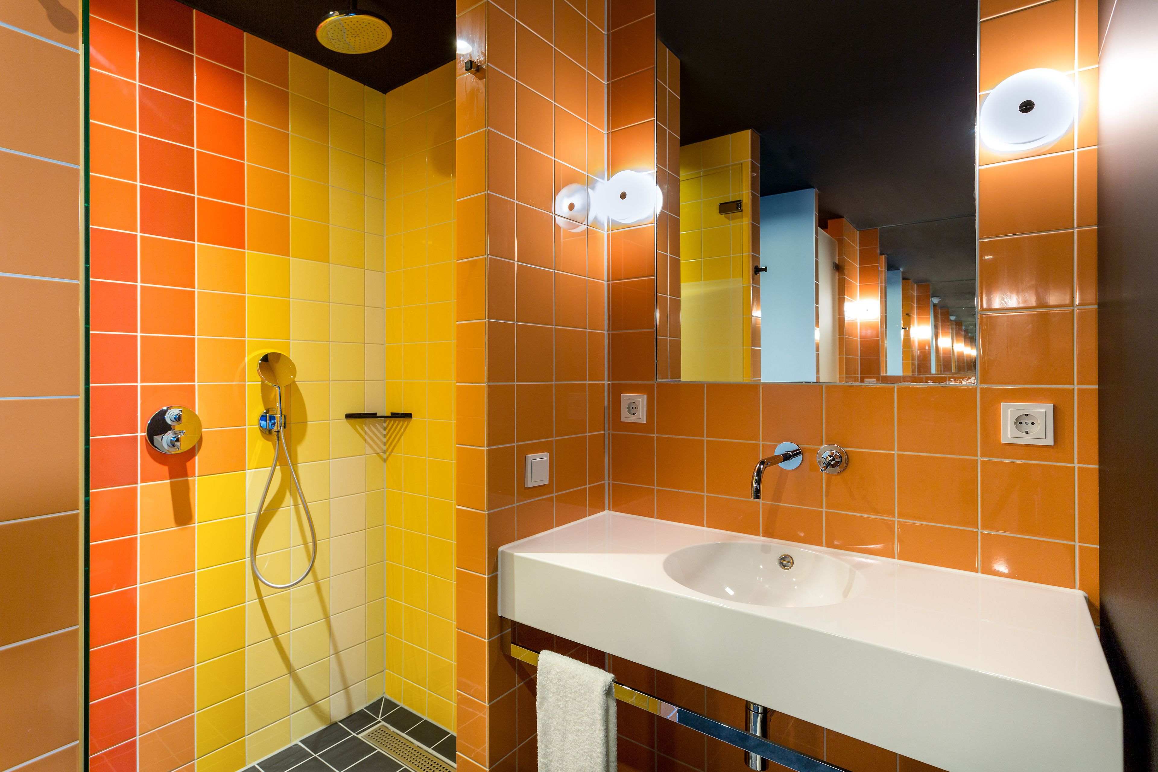 A bathroom with a white sink, a shower, and a mirror reflecting the tiled walls.
