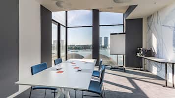 A modern conference room with a large table, blue chairs, and a view of a cityscape through large windows.