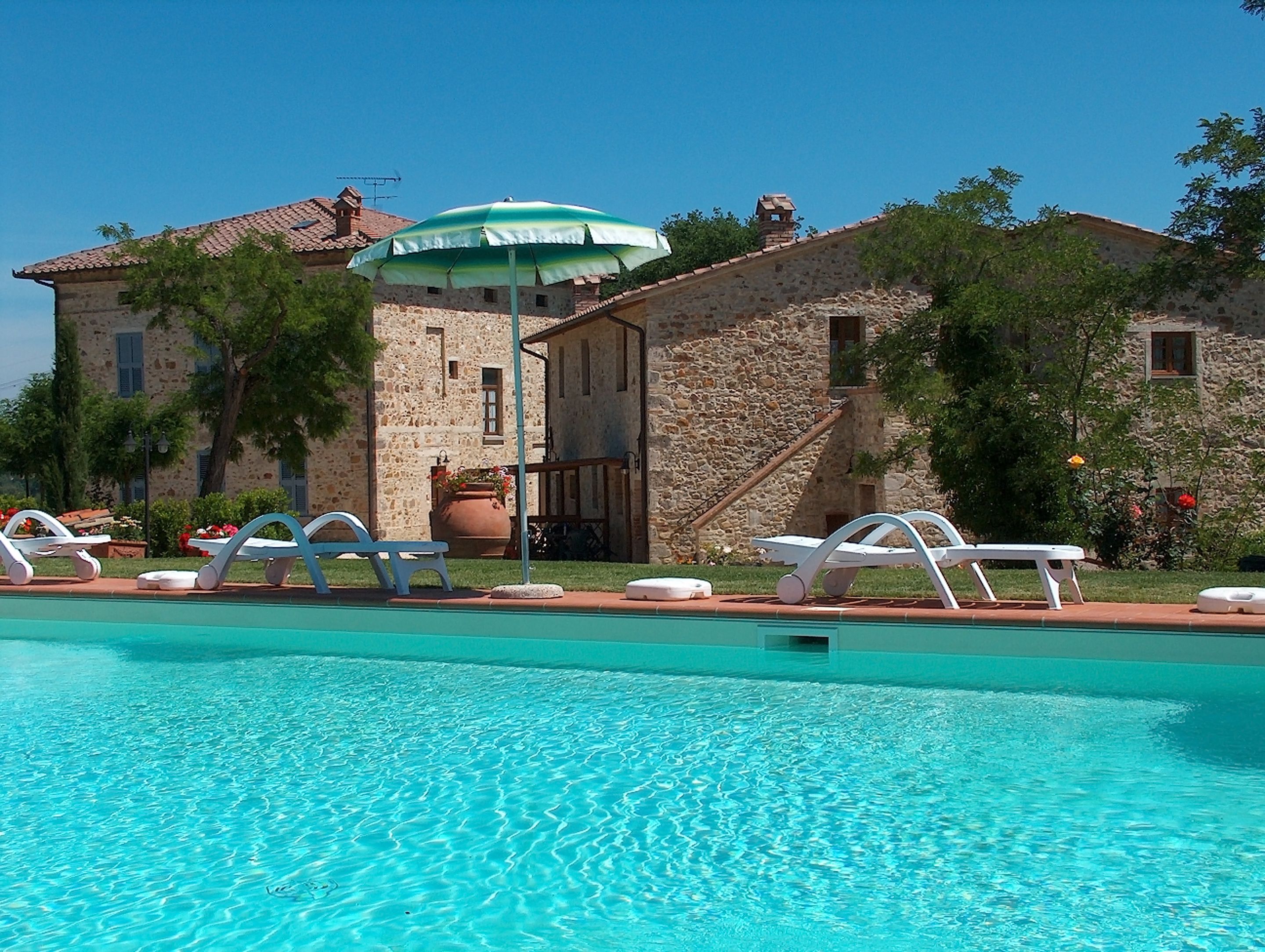 A pool area with lounge chairs and a stone building with a tiled roof.