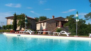 A swimming pool with lounge chairs and a stone building in the background. - Bazzani Apartments (Casole d'Elsa)