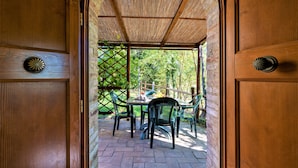 A wooden door with a decorative handle, leading to an outdoor patio with a table and chairs, surrounded by a brick wall and greenery. - Bazzani Apartments (Casole d'Elsa)