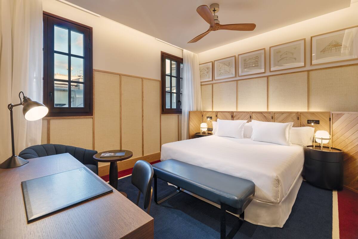 Ein Hotelzimmer mit Bett, Schreibtisch, Stuhl und Deckenventilator.