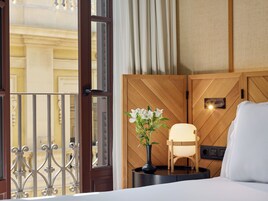 A hotel room with a wooden headboard, a bedside table with a vase of flowers, a chair, and a bed.