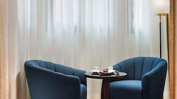 Um quarto com duas poltronas azuis, uma mesinha redonda com um tabuleiro de objetos, e um abajur.