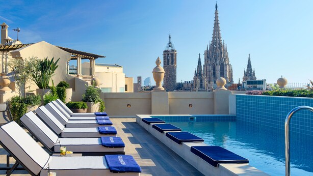 A rooftop pool with lounge chairs and a view of a cathedral. - H10 Madison (Barcelona)
