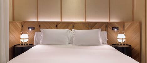 A hotel room with a large bed, wooden headboard, and two bedside tables with lamps.