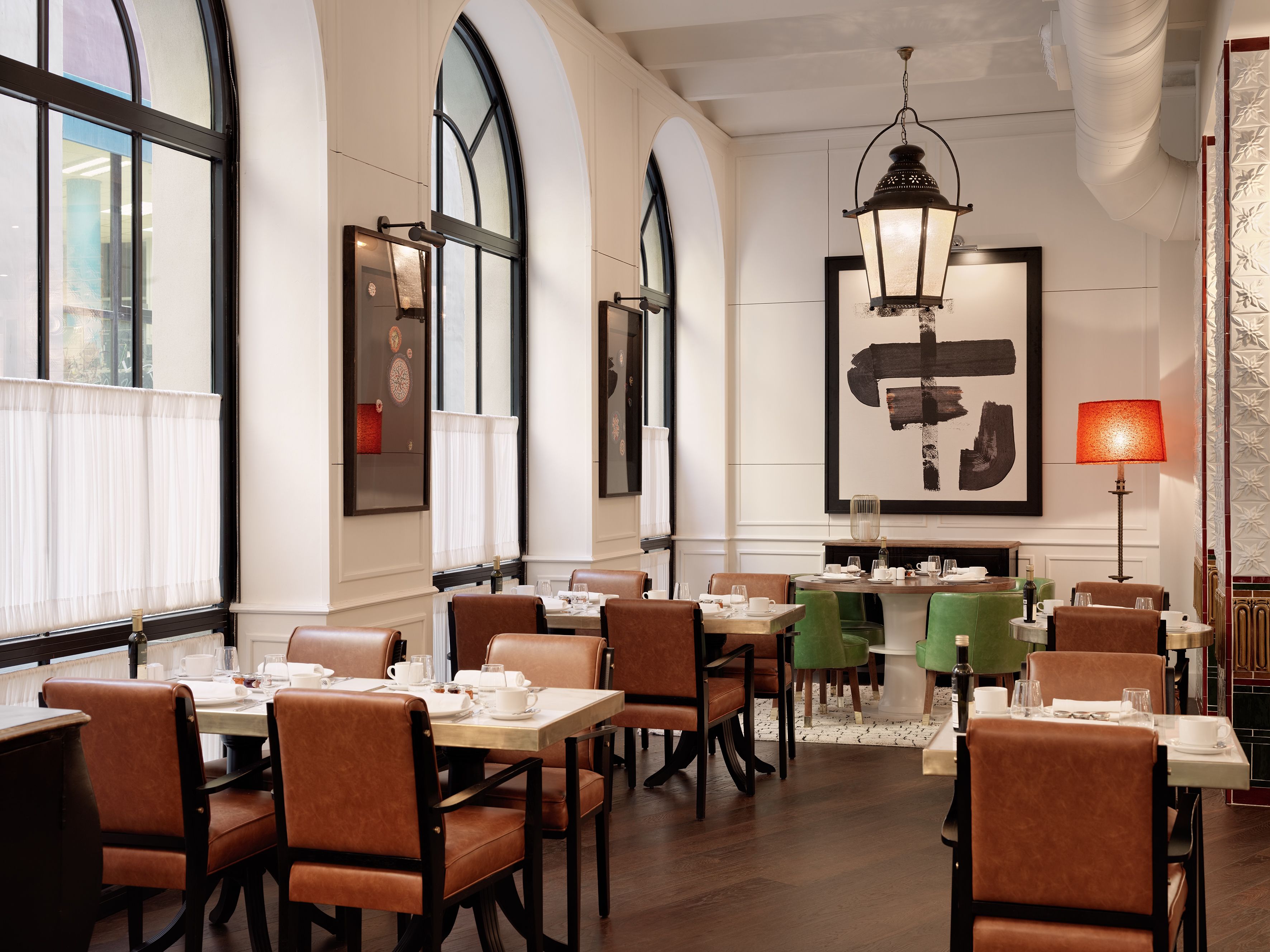 A restaurant with high arched windows, leather chairs, and a central dining table.