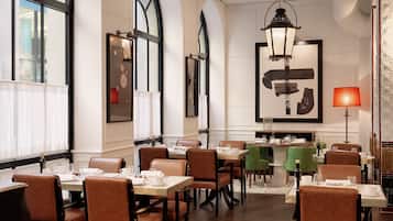 A restaurant with high arched windows, leather chairs, and a central dining table.
