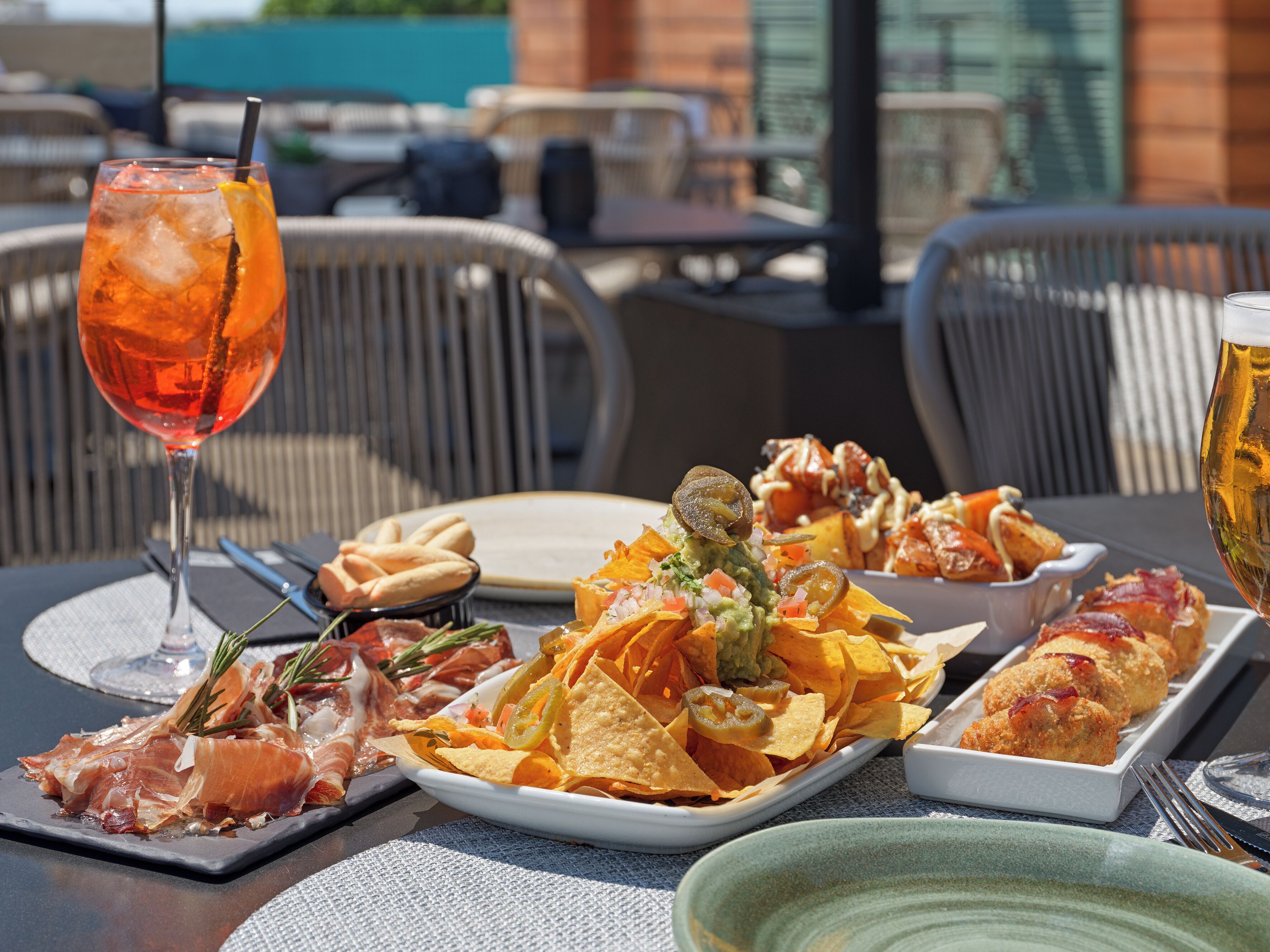 A dining table with a variety of foods including nachos, chips, and meat, along with drinks and a glass of water.