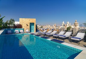 A rooftop pool with lounge chairs, a wooden structure, and a cityscape view.