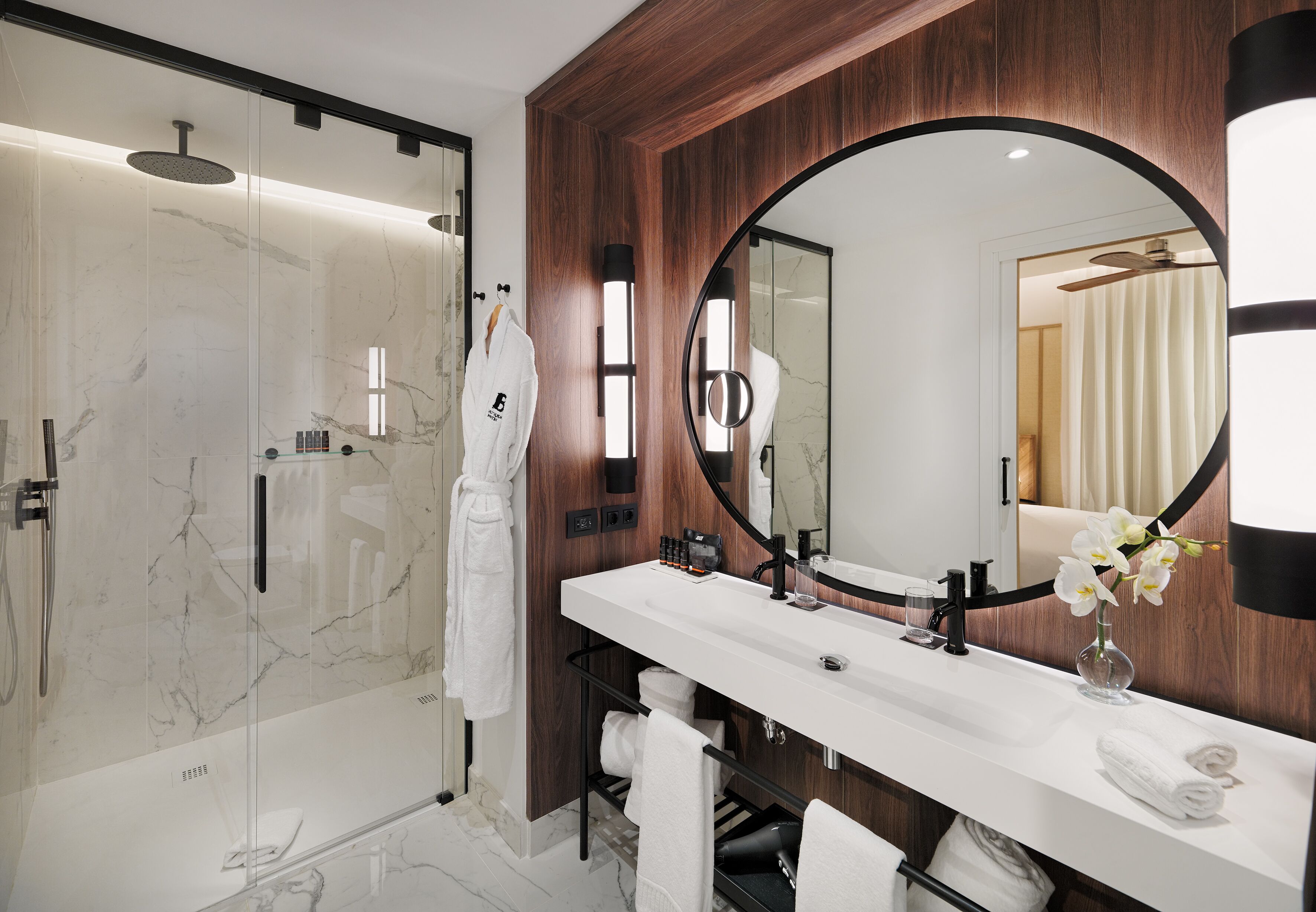 Un baño moderno con ducha envuelta en vidrio, un espejo grande y un mueble de tocador blanco con encimera de mármol.