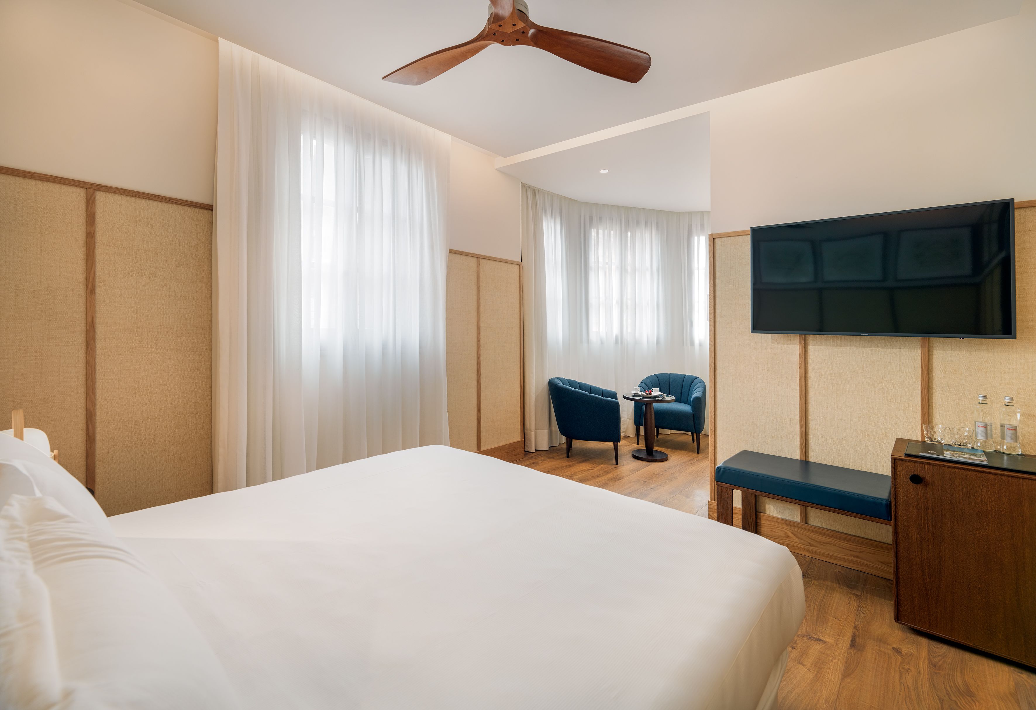 Una habitación de hotel con una cama grande, ventilador de techo, televisión, escritorio y una silla.