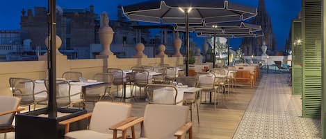 An outdoor seating area with tables and chairs, umbrellas, and a patterned floor.