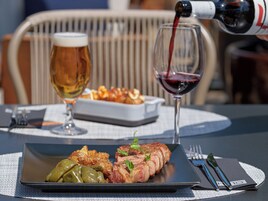 A dining table with a plate of food, a glass of beer, and a glass of red wine being poured.