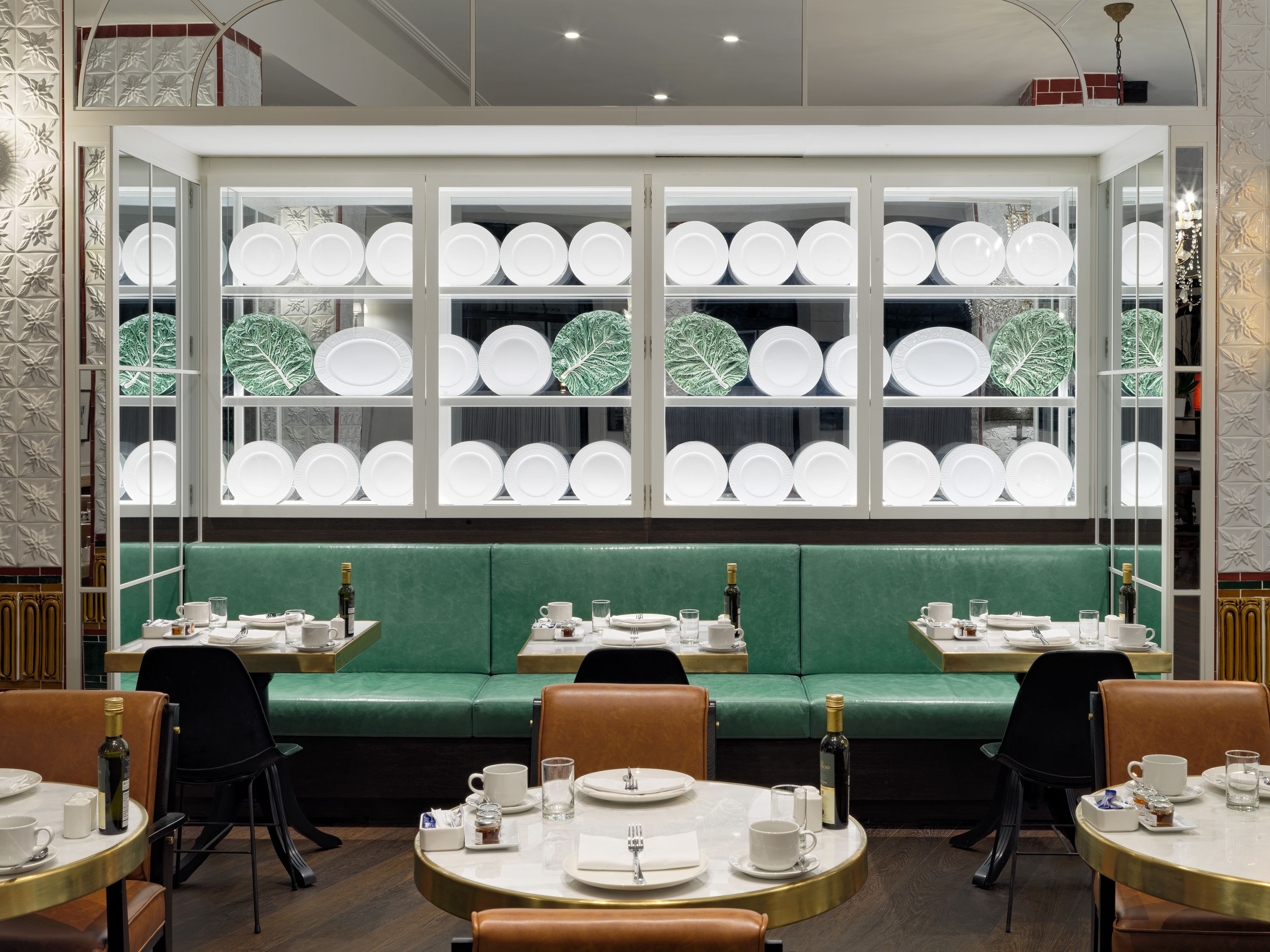 A restaurant with a green booth seating area, white plate display, and round tables with chairs.