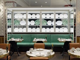A restaurant with a green booth seating area, white plate display, and round tables with chairs.