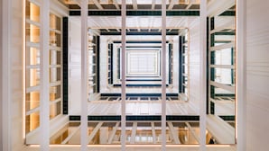 A modern interior with a central open space framed by white columns and glass railings, creating a symmetrical pattern. - H10 Madison (Barcelona)