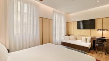 Habitación de hotel con una cama grande, un escritorio con silla, un televisor montado en la pared y un ventilador de techo.