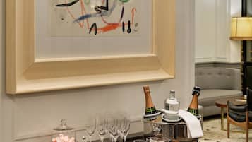 A framed abstract painting on a wall, a wooden sideboard with glasses and bottles, and a grey sofa in the background.