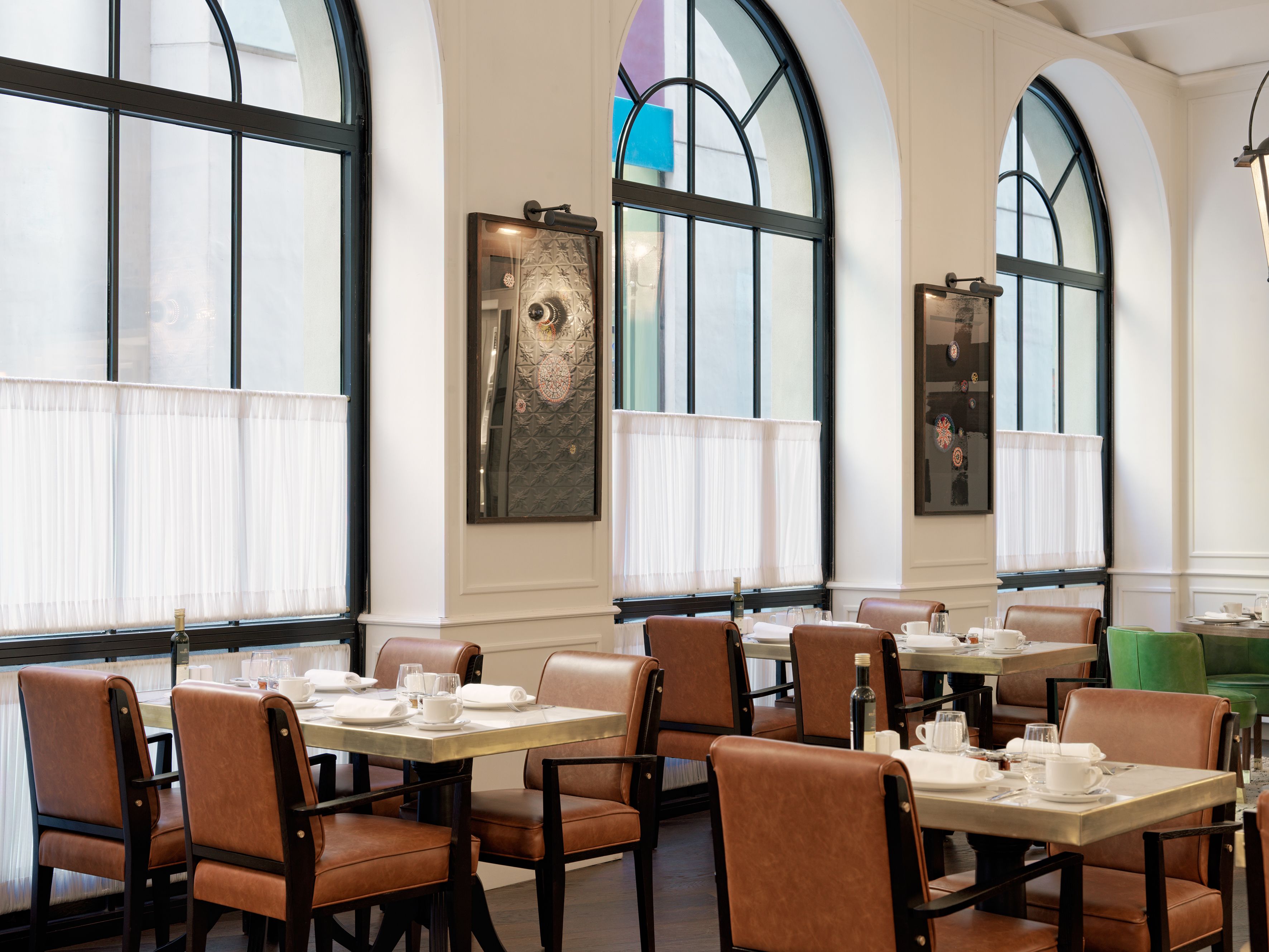 A restaurant with high arched windows, leather chairs, and tables set for dining.