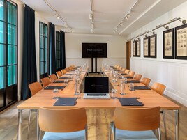 Ein Konferenzraum mit einem langen Tisch, Stühlen, Laptops, Wasserflaschen und einem Bildschirm, der "H10 madison" anzeigt.